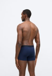 Tumesinised bokserid ruudulise mustriga, valmistatud pehmest kangast, millel on elastne vöökoht ja keha järgnev lõige, rõhutades mugavust.