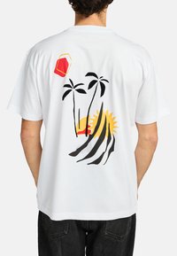 Witte katoenen t-shirt met een kleurrijk grafisch ontwerp van palmboom, een zon en abstracte vormen in rood, geel en zwart op de achterkant.