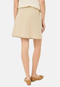 Beige A-linje kjol tillverkad av lätt tyg, med en rak fåll, slät textur och en enkel design, kombinerad med bruna glid-på-skor.