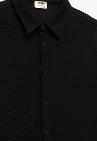 Zwarte poloshirt van een gestructureerde stof, met een klassieke kraag en vijf knopen aan de voorkant, gelabeld "Koton Kids."