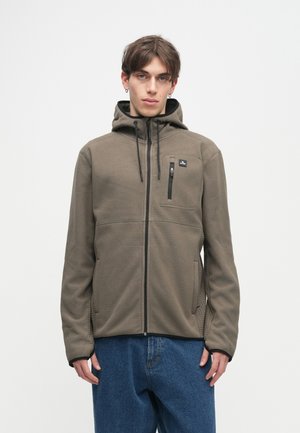 Hættejakke i khaki stof med en tekstureret overflade. Har en frontlynlås og en brystlomme med en kontrastlynlås. Casual pasform.