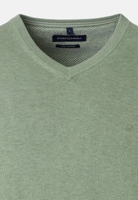 Vaaleanvihreä V-pääntie neulepaita, joka on valmistettu Pima-puuvillasta. Siinä on sileä pinta ja pieni logo alareunassa oikealla puolella.