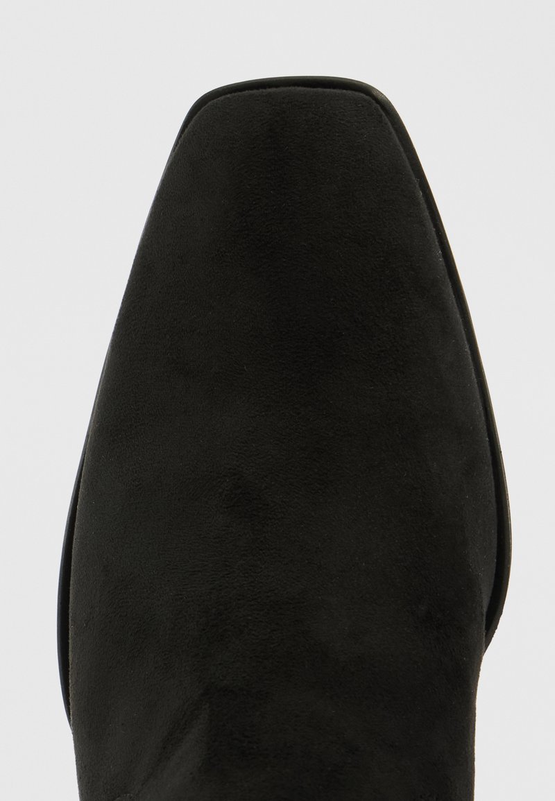 Zapato de ante negro con puntera afilada, textura suave y diseño minimalista. Presenta una suela delgada y líneas limpias.