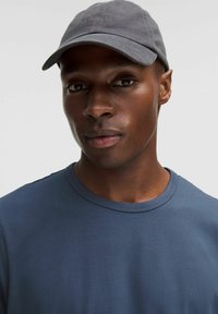 Casquette grise avec logo brodé, associée à une chemise à manches courtes bleue. Tissu lisse, coupe décontractée, avec un col rond.