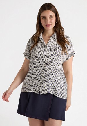 Camisa de manga corta abotonada en crema con un patrón geométrico en azul y marino. Cuenta con un corte relajado y dobladillo curvado. Combinada con una falda de color marino.