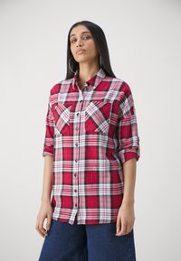 Chemise à carreaux rouge, noir et blanc avec des manches longues, un devant à boutons, deux poches poitrine et un ourlet incurvé. Fabriquée en tissu de coton.