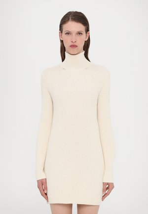 Robe en tricot à col roulé en doux tissu beige, dotée de manches longues, d'une coupe ajustée et d'une texture côtelée sur l'ensemble. Aucun motif ni quincaillerie visibles.