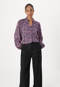Purple floral blouse with bell sleeves and a v-neck, paired with high-waisted black wide-leg pants. Smooth texture, button closure detail.