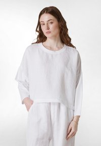 Witte linnen top met een cropped ontwerp, brede mouwen en een ronde hals. Soepele textuur, gecombineerd met bijpassende witte linnen broeken.