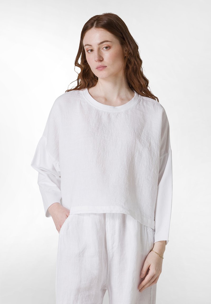 Witte linnen top met een cropped ontwerp, brede mouwen en een ronde hals. Soepele textuur, gecombineerd met bijpassende witte linnen broeken.
