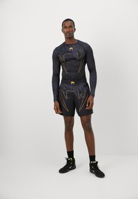 Haut de compression sportif noir avec des accents jaunes et un short assorti, arborant un motif géométrique et un design minimaliste.
