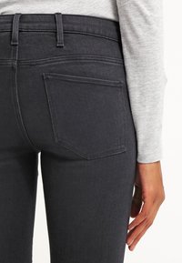 Los jeans de mezclilla negra presentan una textura suave, una cintura alta y dos bolsillos traseros. El tejido muestra un ligero estiramiento y durabilidad.