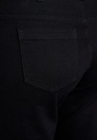 Jeans neri con una texture liscia, dotati di una sola tasca posteriore con cuciture rinforzate. Il tessuto appare resistente e aderente.