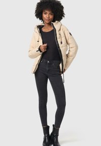 Beige puffer jacket with a hood, black zipper and accents, and a smooth texture. Black fitted jeans and ankle boots complete the outfit.
