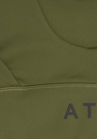 Olijfgroene stof met gedetailleerde stiksels en gedeeltelijke zwarte tekst "AT" aan de rechteronderzijde, met zichtbare stoftextuur en naadontwerp.