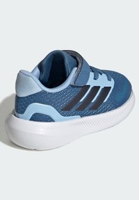 Sinine sportlik jalanõu võrgukangast pealisega, mustate kolmiktriipudega ja valge kummist tallaga. Varustatud velcro rihmadega reguleeritava sobivuse jaoks.