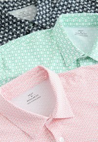 Tři košile s límečkem: námořnická modrá s bílým vzorem palem, zelená s geometrickým vzorem a růžová s červeným geometrickým designem. Všechny mají štítky s běžným střihem.