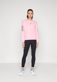 Sweatshirt rose avec "ENDLESS" imprimé sur la manche, associé à des leggings noirs et des chaussures blanches avec des accents bleus.