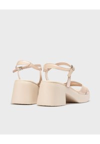 Sandales à talons compensés nudes avec un dessus en cuir lisse, bride ajustable à la cheville et design ouvert; semelle intérieure texturée pour le confort.