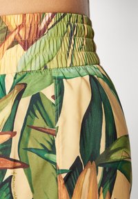 Elastic waist shorts featuring a vibrant floral print with green leaves and yellow accents. The fabric is smooth with a slight sheen.