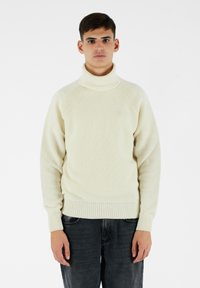 Maglione lavorato a maglia color crema con colletto alto, polsini e bordo a costine, caratterizzato da una finitura texture e maniche raglan.