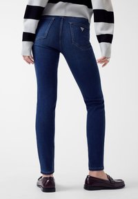 Jean skinny en denim bleu foncé avec poches arrière et petite étiquette logo. Assorti à un pull rayé et des chaussures foncées.