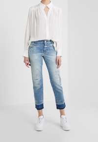 Camisa blanca tipo casual con cuello, combinada con jeans claros desgastados y zapatillas blancas. Tejido suave, corte relajado, dobladillos ajustados.