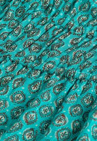 Tissu turquoise avec motifs cachemire marron et crème et texture froncée créant de doux plis.