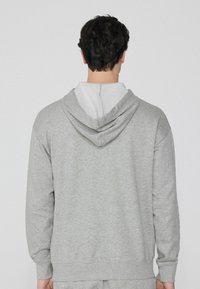 Grauer Kapuzenpullover mit einem kontrastierenden, hellgrauen Innenfutter. Er verfügt über ein strukturiertes, weiches Material und gerippte Bündchen an den Handgelenken und am Saum.