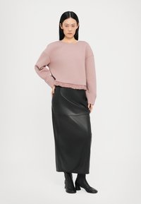 Felpa corta rosa chiaro con orlo volants, abbinata a una lunga gonna di pelle nera. Stivali neri con tacco completano il look.
