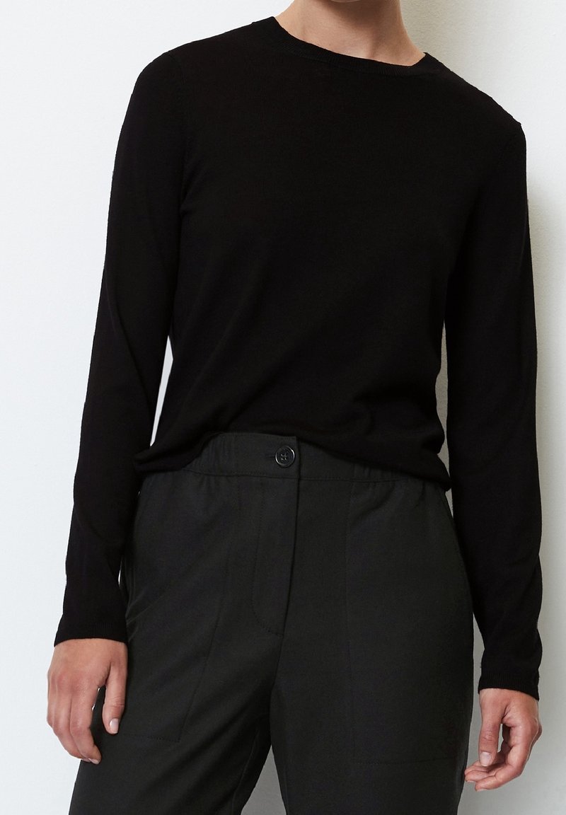 Zwarte, lange mouwen trui gemaakt van een zacht gebreid materiaal met een klassieke ronde hals, gecombineerd met donkere, op maat gemaakte broek met een knoopsluiting.