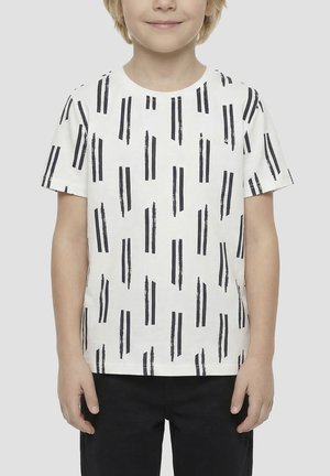 Kind dat een wit T-shirt met korte mouwen draagt met verticale zwarte penseelstreekpatronen en een zwarte broek, staand tegen een effen achtergrond.