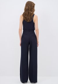 Marina vida byxor med hög midja och bälte, med en slät textur och en bakficka, parat med en figurnära marinblå linne.