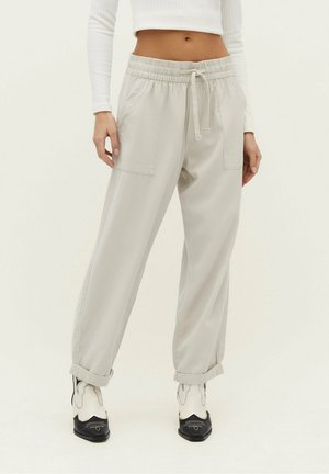 Slanke persoon met een lichte beige broek met koordsluiting en opgerolde pijpen, gecombineerd met zwart-witte westernlaarzen.