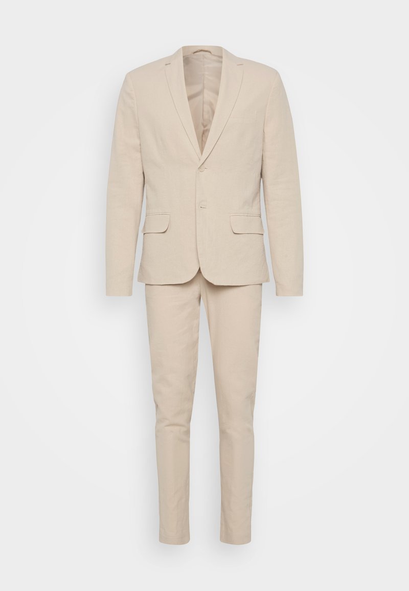 Costume en lin beige comprenant un blazer à deux boutons avec des revers en pointe, des poches latérales et un pantalon slim-fit. Texture lisse, détails minimaux.