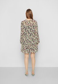 Blumenkleid mit schwarzem Hintergrund, das mit rüschierten Schichten, langen Ärmeln und einem runden Ausschnitt versehen ist. Kombiniert mit mintgrünen Riemchen-High-Heels.