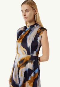 Ärmelloses Kleid aus mehrfarbigem Stoff mit abstrakten Mustern in Blau, Gold und Schwarz. Hoher Kragen mit glatter Textur.
