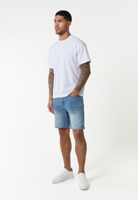 Weißes Baumwoll-T-Shirt, hellblaue Denim-Shorts und weiße Sneaker. Das Shirt hat einen Rundhalsausschnitt; die Shorts verfügen über Seitentaschen und eine lockere Passform.