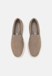 Chaussures Clarks à enfiler en daim marron avec une texture lisse, un bout arrondi et une semelle en caoutchouc claire. Présentent une couture minimale et une ventilation.