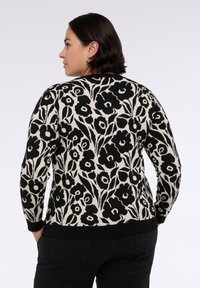 Maglione lavorato a maglia con motivo floreale nero e crema, maniche lunghe, scollo tondo e orlo a coste. Vista posteriore che mostra design e struttura dettagliati.