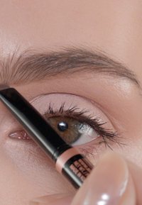 Zwarte wenkbrauwpotlood wordt gebruikt om de wenkbrauwen in te vullen. Close-up van een bruine oog met lange wimpers, een lichte huidtint en een zachte make-up.