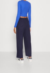 Blå randig långärmad cropped topp som matchas med lösa marinblå byxor och svart-vita sneakers. Slät yta med elastisk midja.