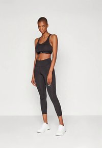 Reggiseno sportivo nero e leggings a vita alta, realizzati in tessuto liscio ed elastico, con design elegante e dettagli con logo. Scarpe da ginnastica bianche.