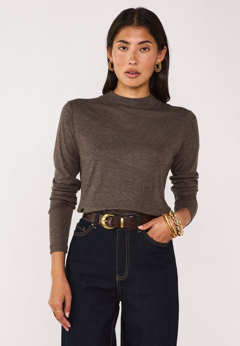 Maglia marrone a maniche lunghe con collo alto, realizzata in tessuto testurizzato, abbinata a jeans a vita alta blu scuro e una cintura marrone con fibbia dorata.