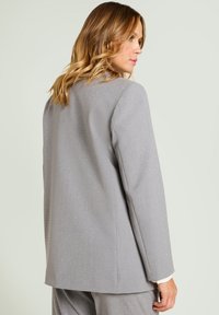 Blazer gris de diseño estructurado, fabricado con tejido texturizado con un sutil patrón de puntos. Presenta hombros relajados y mangas largas.