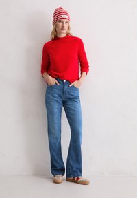 Czerwony sweter z dzianiny w połączeniu z jasnoniebieskimi spodniami dzwonami. Model nosi paskowaną czapkę i casualowe trampki. Prosty design i luźny krój.