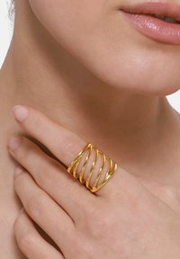 Gouden metalen ring met vijf spiraalbanden, met een gladde, glanzende textuur. De ring is om een vinger gedragen, gedeeltelijk zichtbaar op de afbeelding.