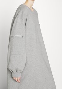 Överdimensionerad grå sweatshirt med rund hals, långa ballongsärmar och en dragkedjeficka på vänster ärm. Mjuk bomullsmaterial.