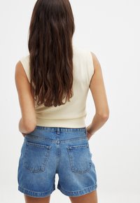 Beige ribbad ärmlös topp i kombination med högmidjade blå denimshorts, med en klassisk skärning och två bakfickor.