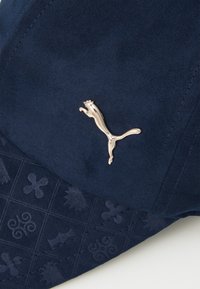 Navy cap with a textured pattern and a metallic gold Puma logo. Features a smooth fabric and structured shape.